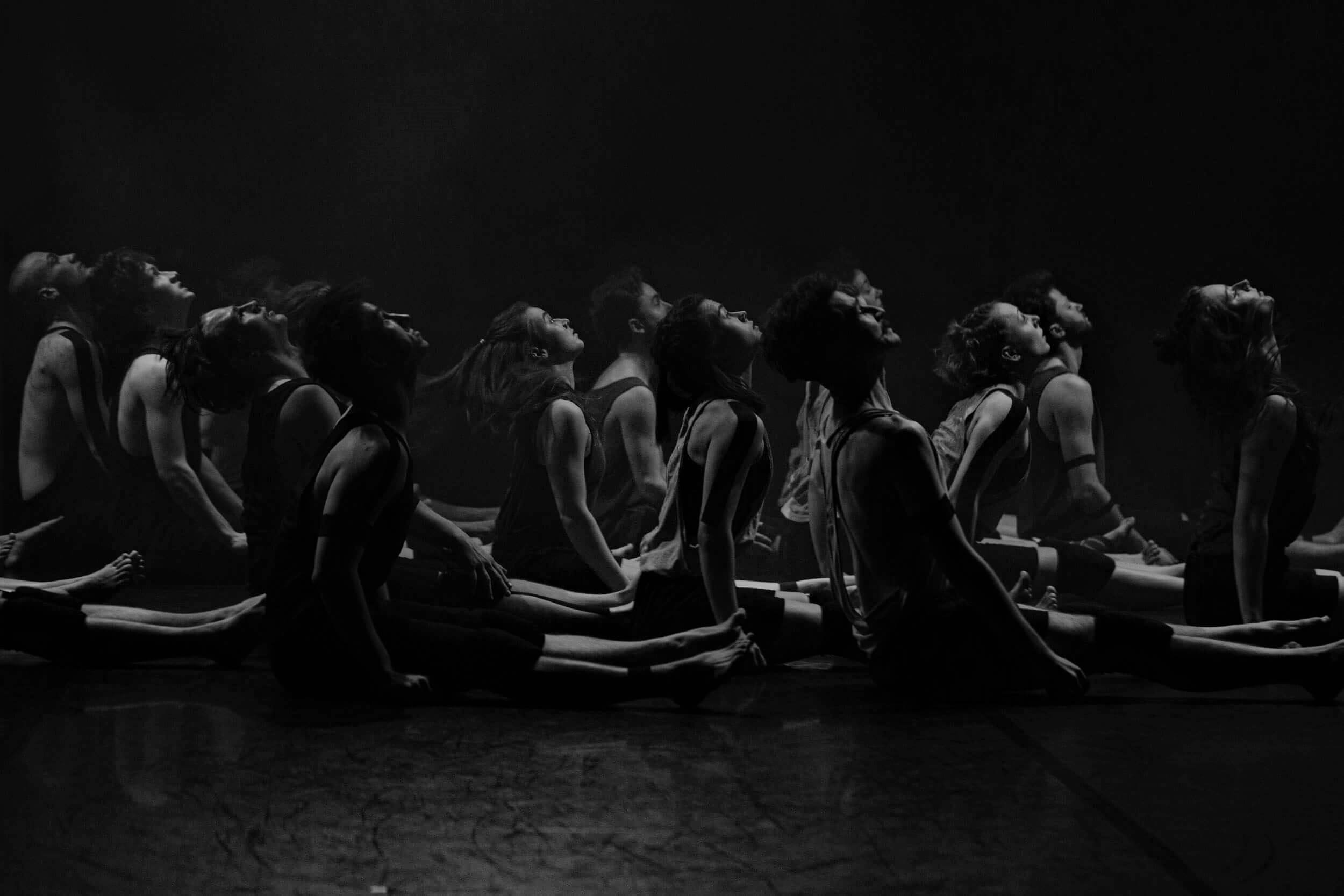 6. Flying fish- czarno-białe zdjęcie, na którym znajdują się siedzący na scenie tancerze, mający skierowane głowy w górę, w stronę świateł.