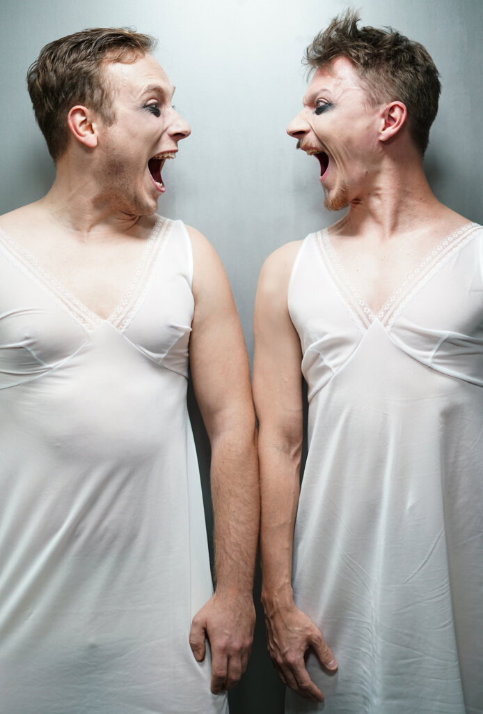 Pionowe zdjęcie, na którym znajduje się dwóch mężczyzn ubranych w białe halki, ich twarze są skierowane na siebie do środka, mają otwarte usta jakby krzyczelitaa