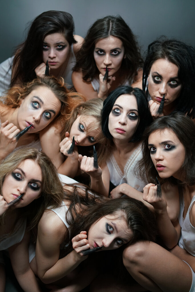 pionowe zdjęcie na którym znajduje się dziewięć dziewcząt,które mają pomalowane oczy na czarno, rozpuszczone włosy i pomalowany na czarno mały palec
