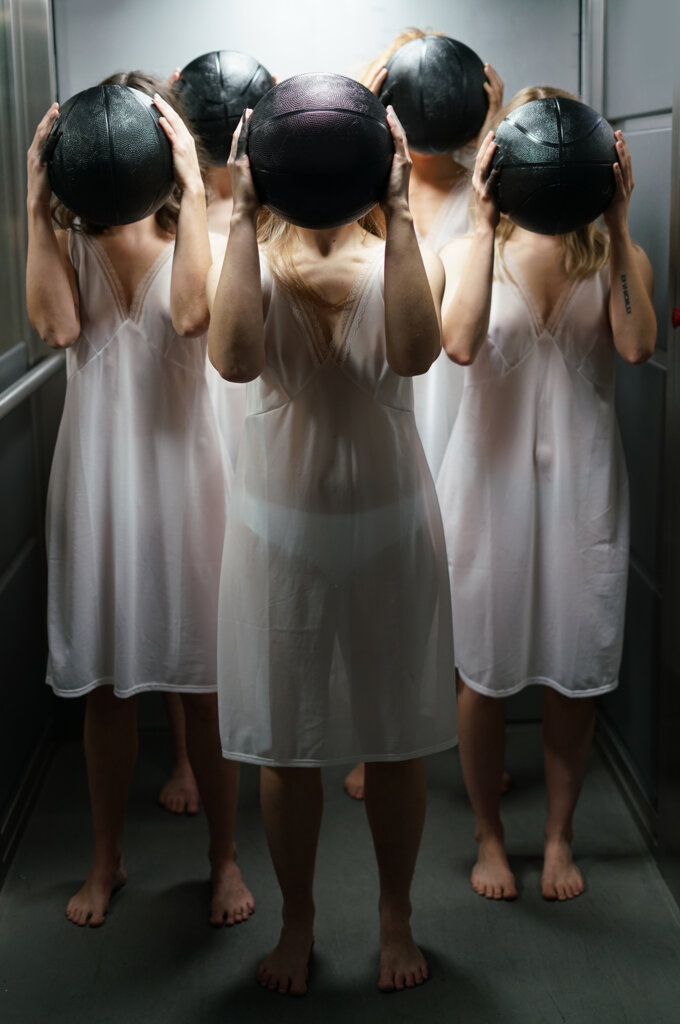 Pionowe zdjęcie na którym znajdują się cztery dziewczyny ubrane w białe halki w rękach na wysokości twarzy trzymają czarne piłki