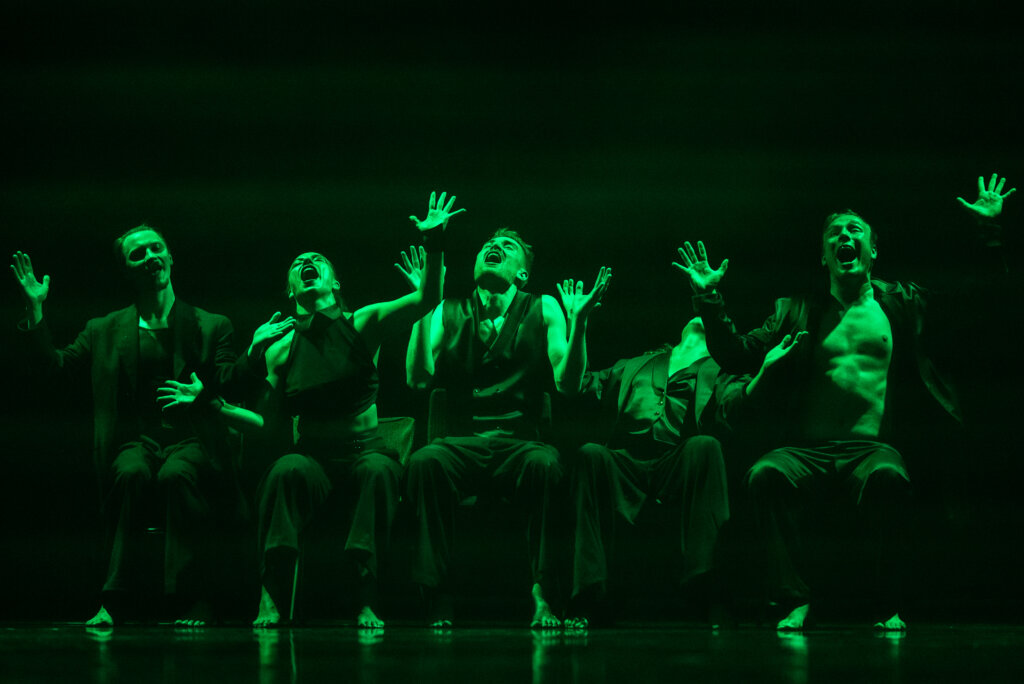 Bestie. Na zdjęciu jest pięciu tancerzy siedzących na krzesłach, mają uniesione ręce w górę, odchylają się do tyłu i mają otwarte usta. Ubrani w czarne stroje.