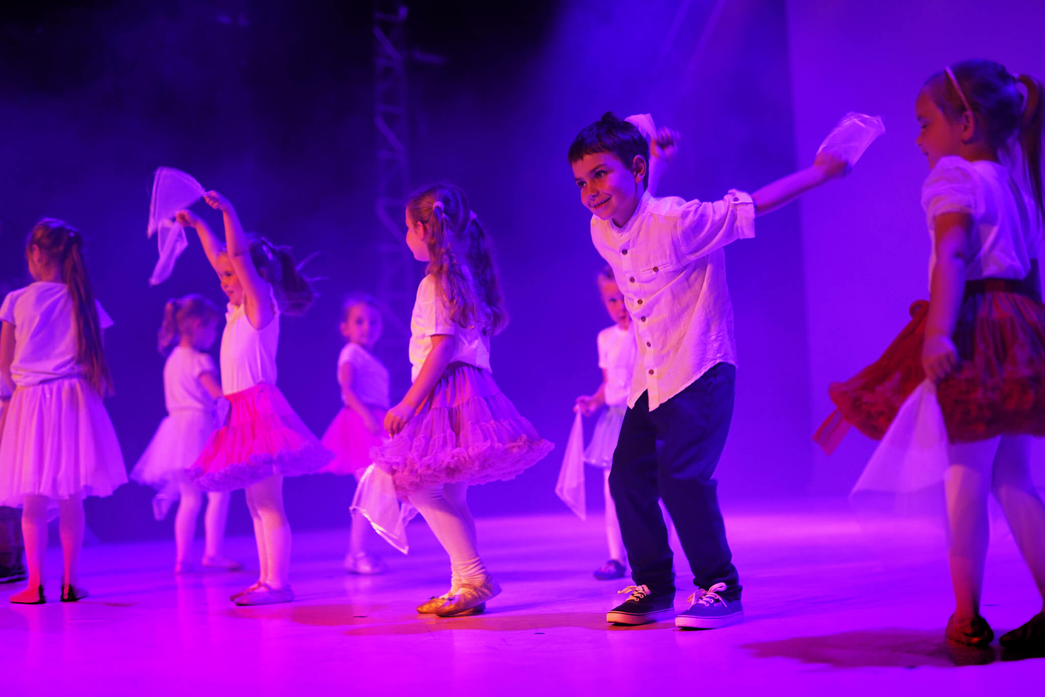 Grupa dzieci w wieku przedszkolnym tańczy z chustami na scenie.